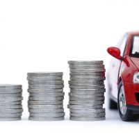 Stacks of giant silver coins next to a new red car